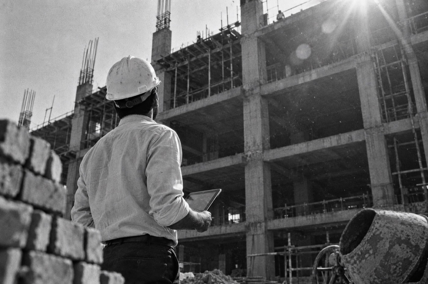 Engineer with a tablet looking up at a building frame